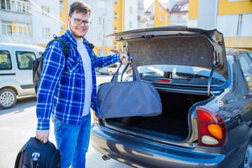 young adult man putting bag in car trunk. car travel concept