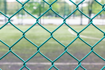 Fototapeta premium Green wire fence and football field on background