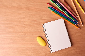 Open notebook on wooden background with colorful pencils and eraser. Flat lay