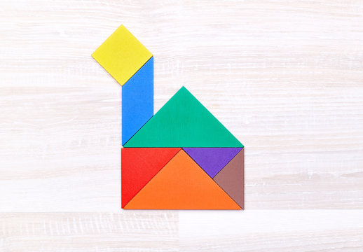 Flay lay of colorful tangram figures arranged in shape of boat on wooden table.