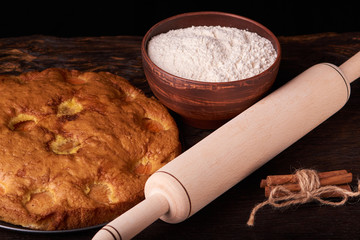 On a dark wooden table, fashionable bakeries, a bowl with flour, apricot cake and tools stand on table
