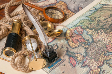 Quill pen on old paper sheets with old rolled maps and vintage items