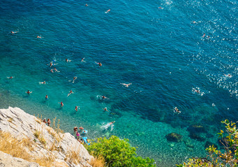The top view and the beach. View from the high rocky shore. Azure-blue clear water. People swim in the beach. Black sea, Crimea