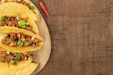 Overhead closeup photo of Mexican tacos with pulled meat, avocado, chili peppers, cilantro, with copy space