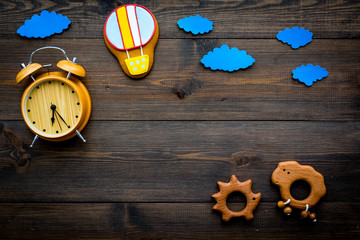 Put baby to bed concept. Childrens toys and clacks, baby accessories, alarm clock, clouds on dark wooden background top view copy space