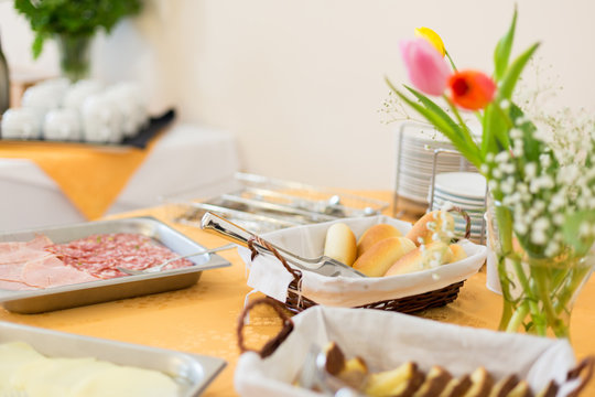 Self-service Breakfast On The Table. Bread In A Wicker Basket, Trays With Cold Cuts And A Vase With Flowers