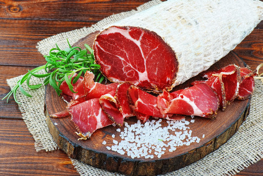 Sliced cured coppa with spices and a sprig of rosemary.