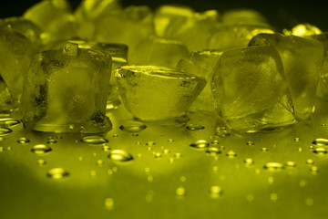 Ice cubes in yellow on a reflecting table with ice drops