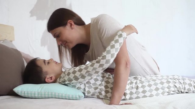 Mom kisses her beloved son while he is lying on the bed and hugs her