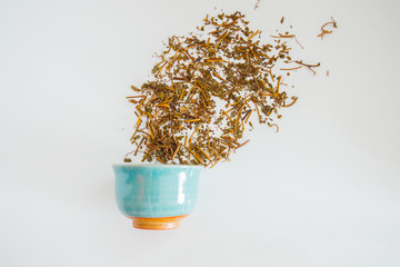Dried tea leaves with a cup of tea on a white background.
