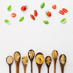Different kind of pasta on wooden spoon and ingredients on white background from top view. Italian food concept.