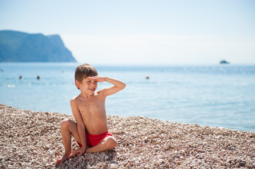 Fototapeta na wymiar handsome little boy watching far sitting on summer beach on tropic remote island