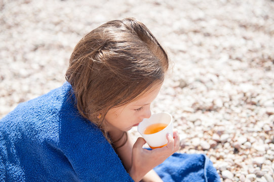 Little Child Wrapped In Blue Towel Drinking Cup Of Tea On Summer Beach Outdoor