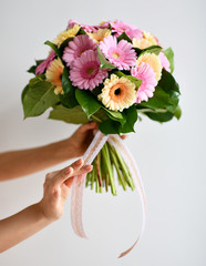 Beautiful woman hands hold bouquet of gerbera flowers pink and yellow on grey