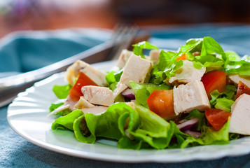 fresh vegetables salad with chicken and onion, lettuce, tomato in white plate on table