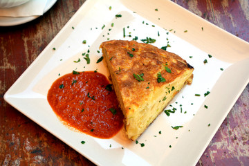 Traditional spanish omelette with hot sauce on a plate. 