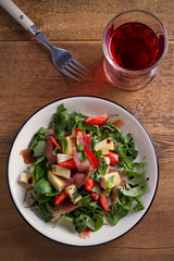 Strawberry, basil, mint, arugula salad with brie cheese and jamon on white plate on wooden table. vertical, overhead