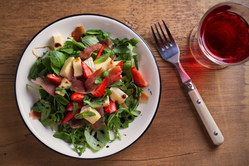 Strawberry, basil, mint, arugula salad with brie cheese and jamon on white plate on wooden table. horizontal, overhead