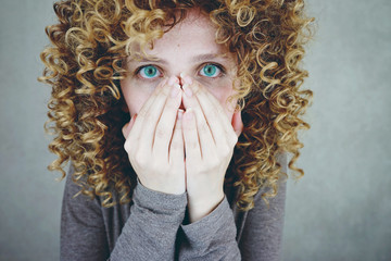 Mujer joven y rubia cubriéndose la cara con las manos 