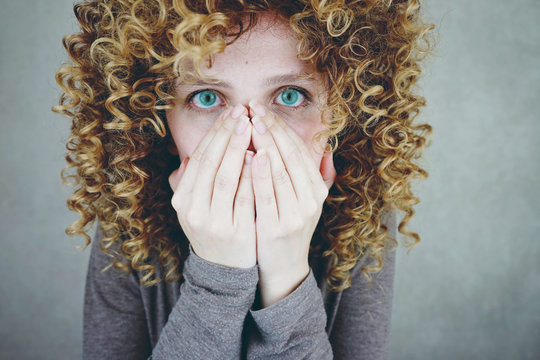 Mujer joven y rubia cubri&eacute;ndose la cara con las manos 
