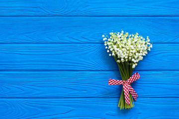 Beautiful bouquet of flowers lily of the valley with red ribbon on blue wooden table/ top view, flat lay, copy-space