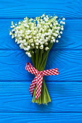Beautiful bouquet of flowers lily of the valley with red ribbon on blue wooden table/ top view, flat lay, copy-space