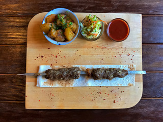 Meat cutlets on skewers and fried potatoes, fresh cabbage and ketchup in bowls on a wooden board