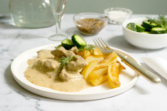 Beef Stroganoff traditional Russian dish of beef in sauce, served with fried potatoes, canned cucumbers, vodka.