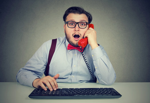 Shocked man speaking on phone at workplace