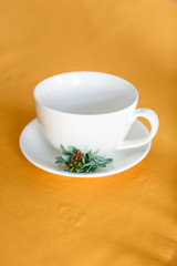 White tea cup empty with saucer on an orange tablecloth, closeup. Small green twig lies on saucer