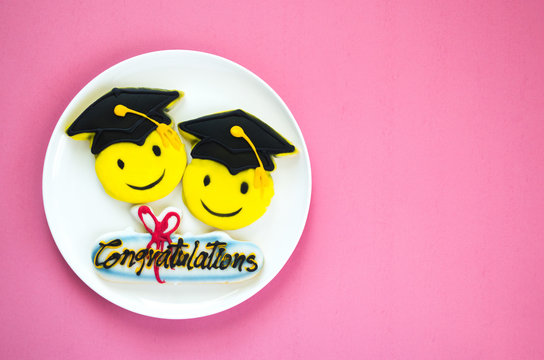 3 colorfully decorated graduation cookies on a white plate against a pink background with copy space