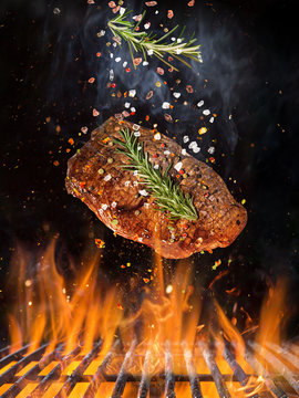 Tasty beef steak flying above cast iron grate with fire flames.