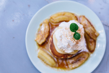 Top view of Pancakes with caramel-banana syrup topping with whip cream and mint leaves.