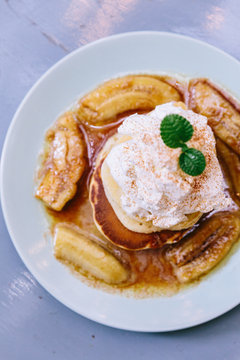 Top view of Pancakes with caramel-banana syrup topping with whip cream and mint leaves.