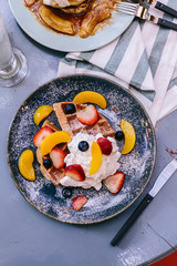 Top view of Fresh baked Pancakes topping with strawberry, orange, blueberry and whip cream with knife.