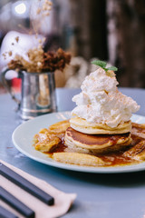 Close up Pancakes with caramel-banana syrup topping with whip cream and mint leaves. With spoon, fork and knife.