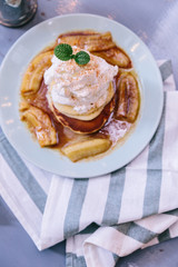 Top view of Pancakes with caramel-banana syrup topping with whip cream and mint leaves. In blue plate over fabric with blue stripes.