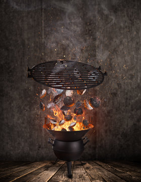 Kettle grill with hot briquettes and cost iron grid flying in the air.