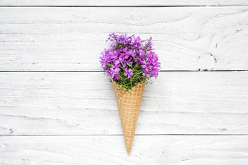 Ice cream cone with purple flowers over white wooden background. top view