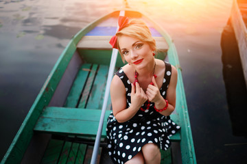 Beautiful young woman dressed dressed in a boat on a lake shore