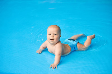 Fototapeta na wymiar Happy, smiling little baby boy lying in blue swimming pool in water.