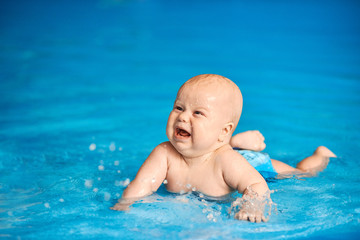 Fototapeta na wymiar Funny little baby boy lying in blue pool. Active lifestyle of child.