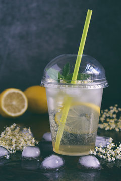 Homemade elderflower lemonade with lemon and elderberry flowers in plastic cup with sphere dome cap and cocktail tube. Elderflower cordial. Summer cold drink