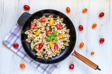 Cast-iron frying pan with farfalle aglio olio and cherry tomatoes