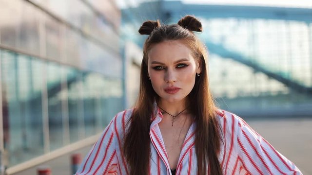 Stunning fashion model with a hair-do and in red sunglasses stands before a glass wall and poses for the camera
