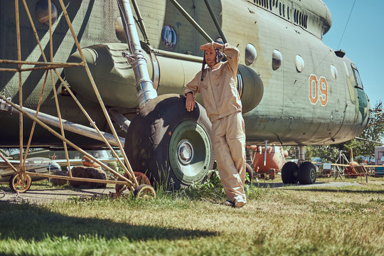 Mechanic in uniform and flying near the large military helicopter while leaning on a chassis in an open-air museum.