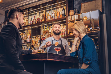 Cheerful stylish brutal barman serves an attractive couple who spend an evening on a date.