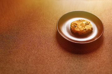 The cookie lies on a plate. Sunlight. Brown background. Text place