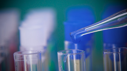 Pipette with the analysis and DNA, drip small drops in test tubes, dark green background, macro.