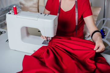  A seamstress woman in red clothes sews on a sewing machine. Atelier, the process of tailoring.